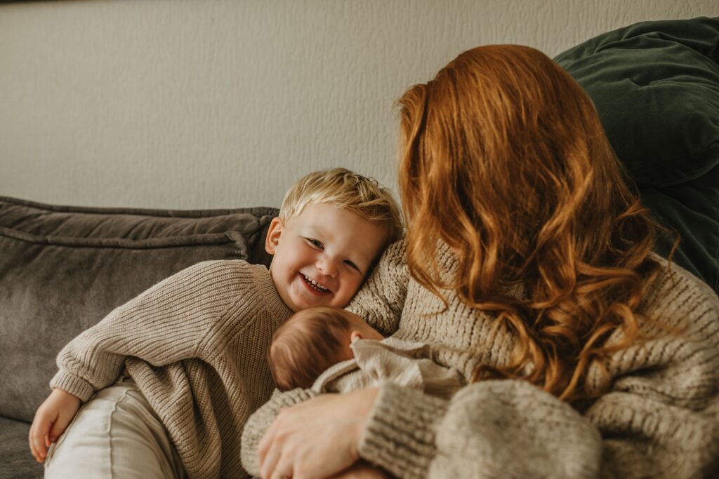 Wanneer een babyshoot shot van moeder met pasgeboren baby en het broertje op de bank.